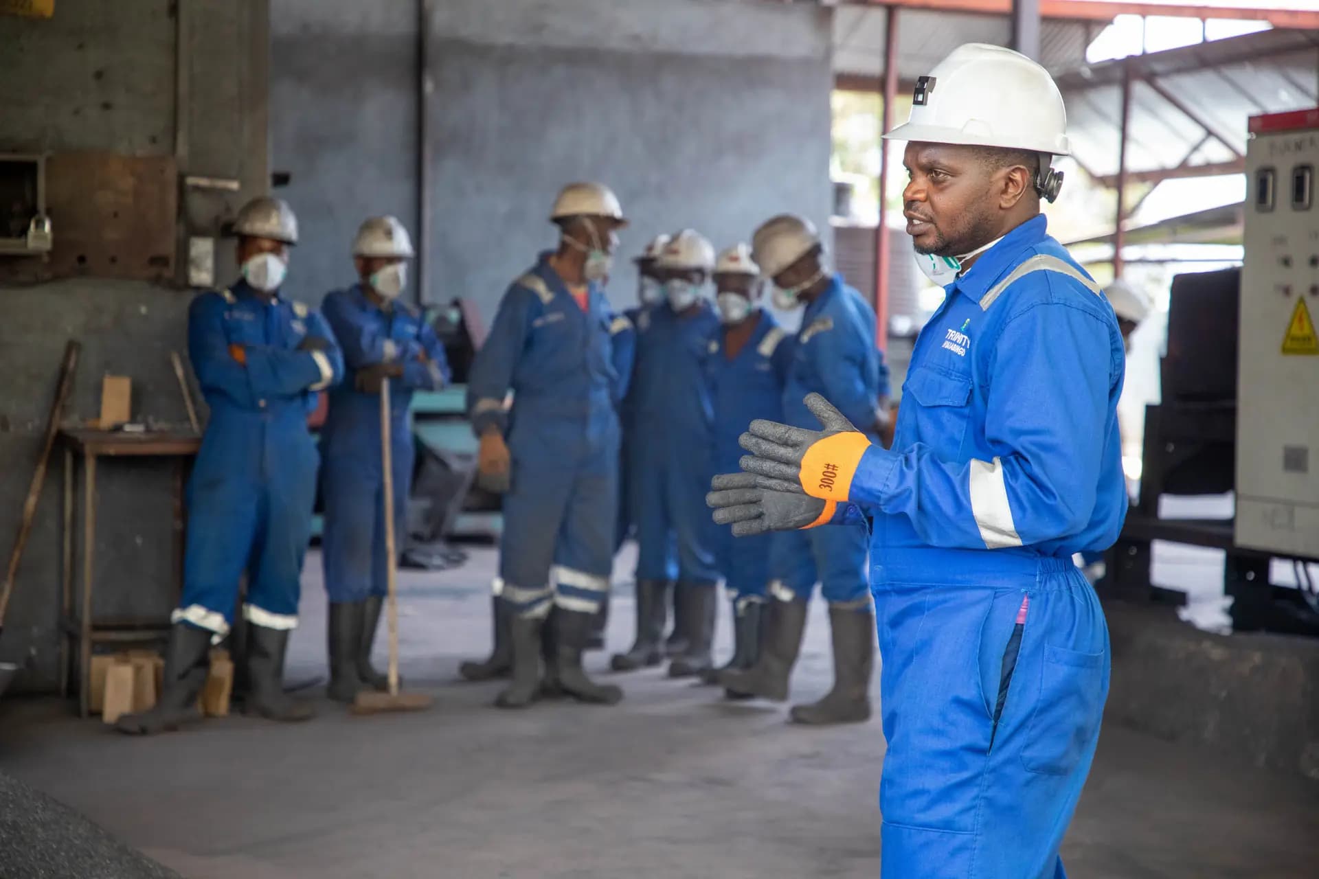 Instructor in a hard hat leading a group of workers in overalls on a factory floor