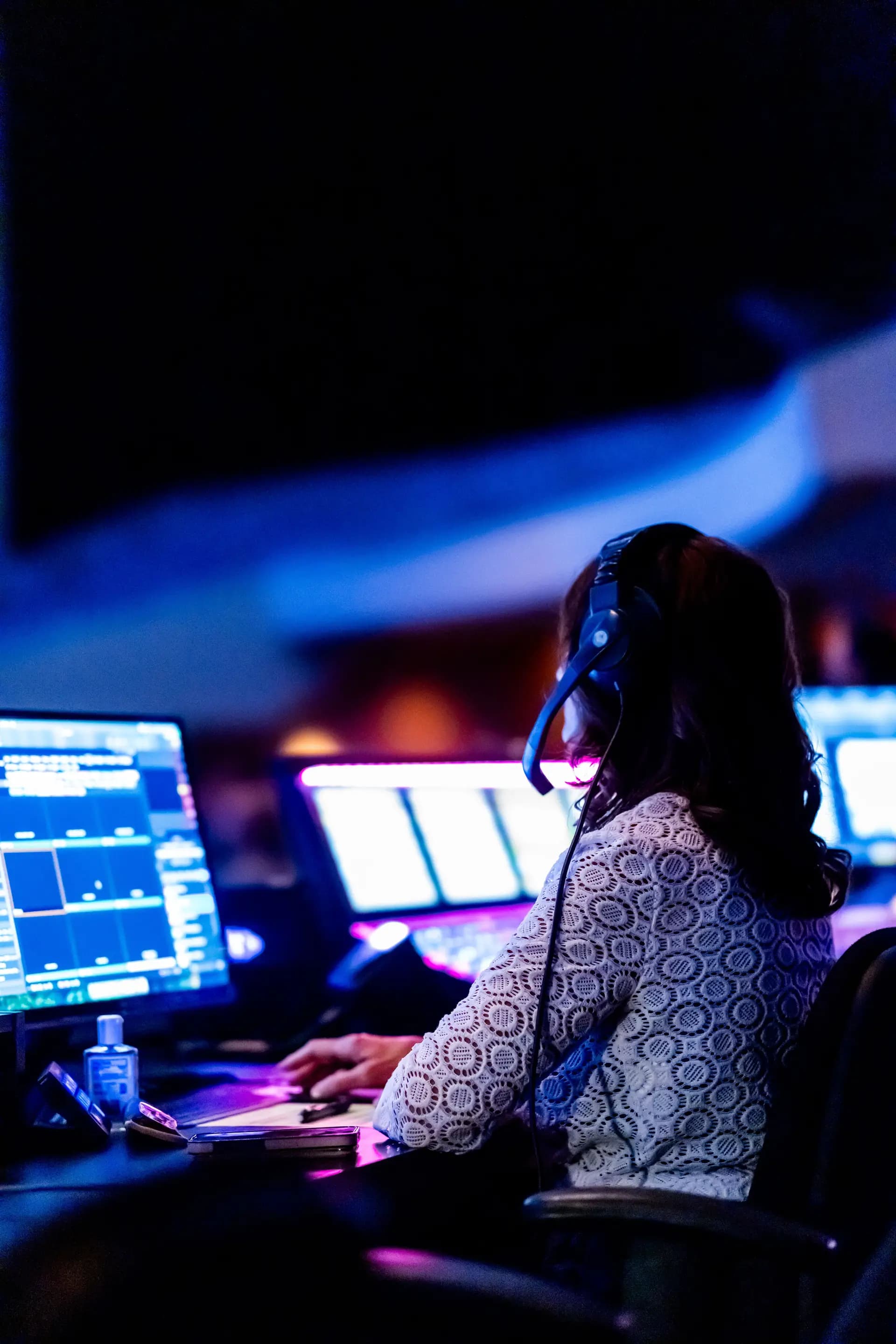 Woman wearing a headset in front of glowing monitoring screens in a dark control room
