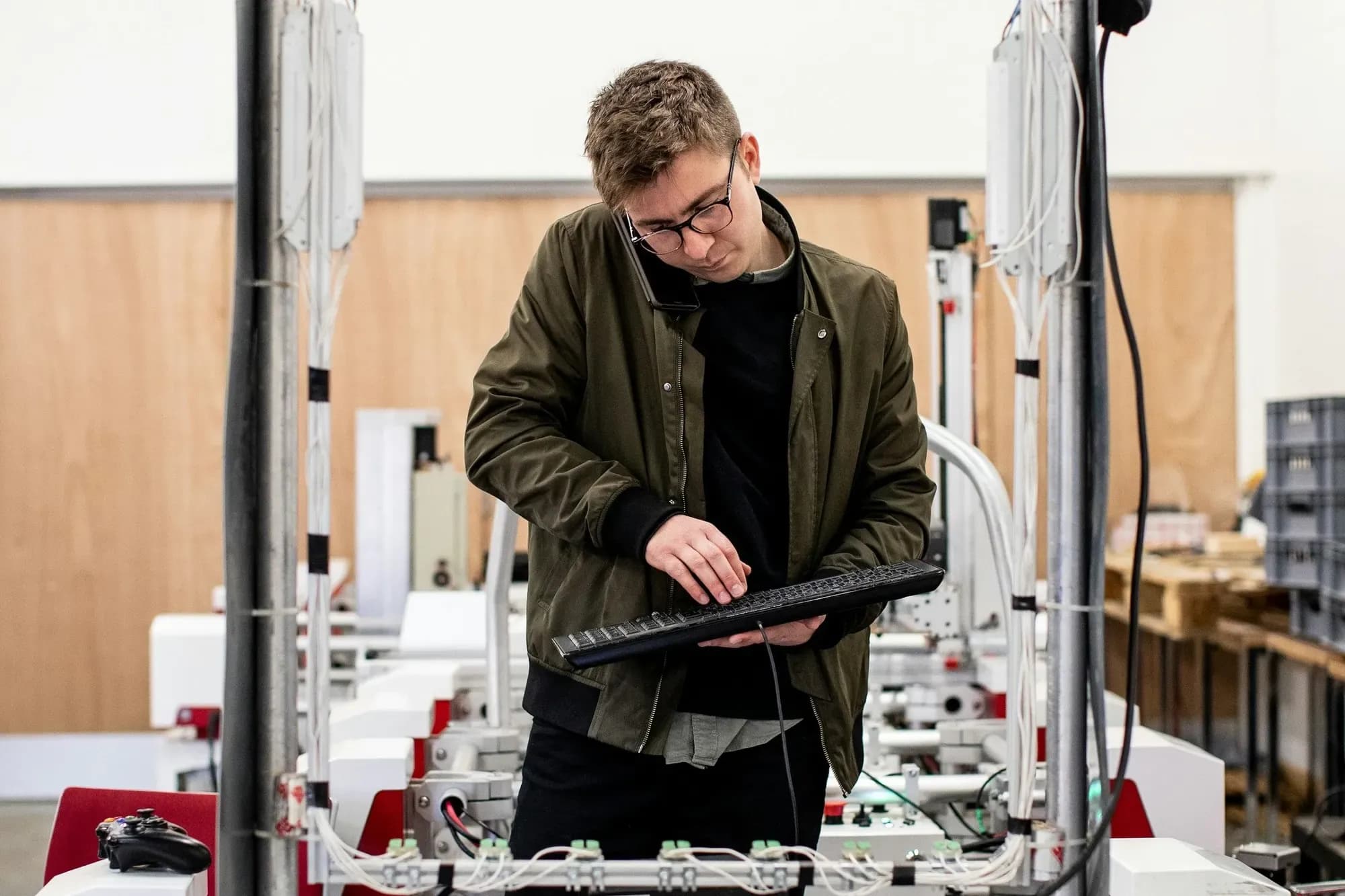 Automation engineer in an olive jacket holding a tablet beside a test rig in a training workshop