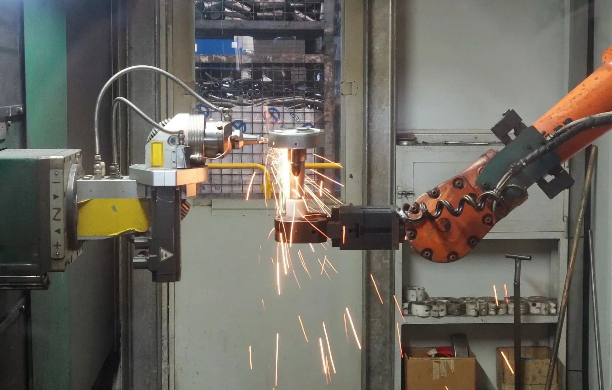 Orange industrial robot arm holding a part against a grinding tool and throwing sparks