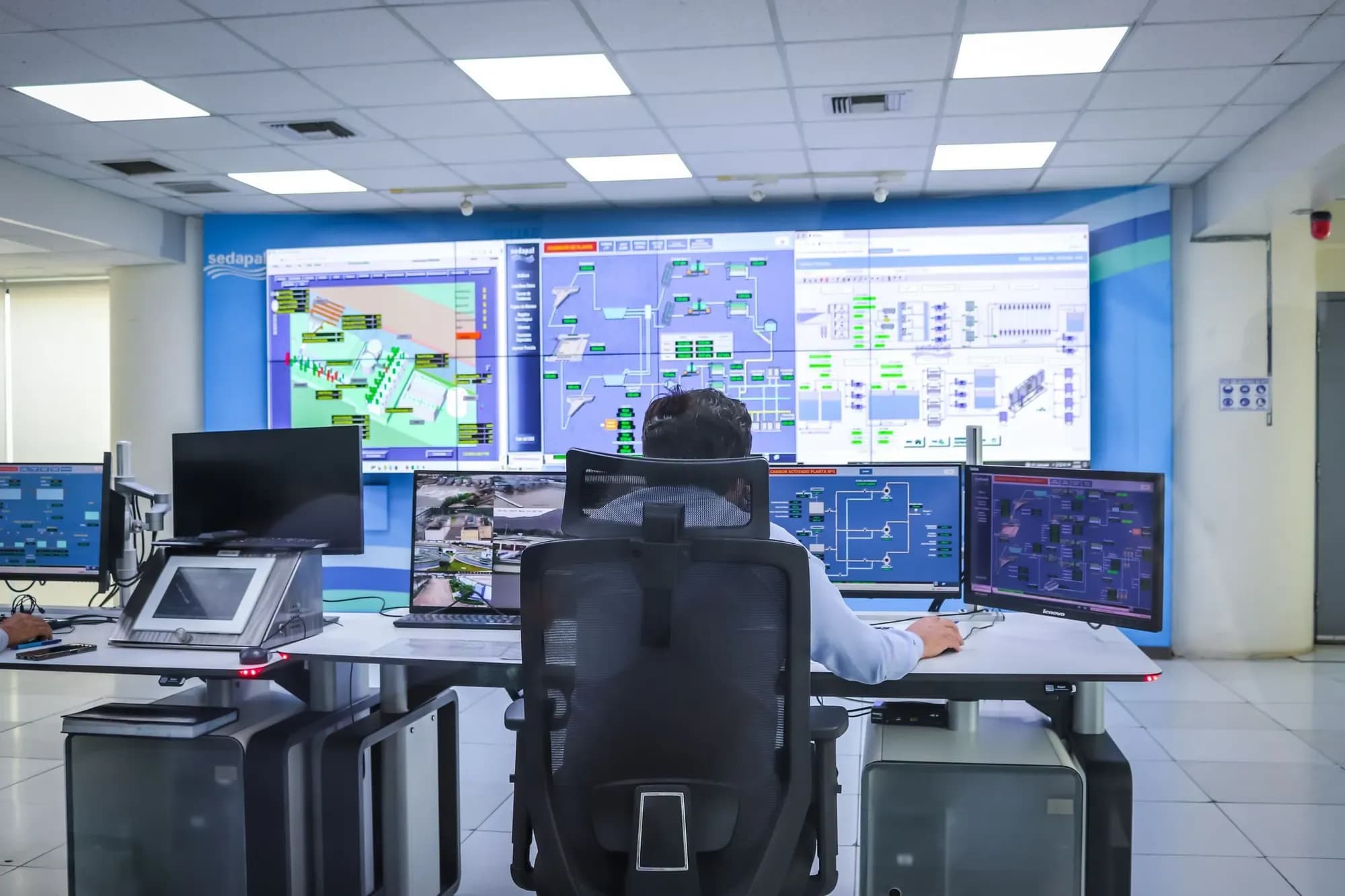 Operator at a desk in a modern control room facing a video wall of process screens