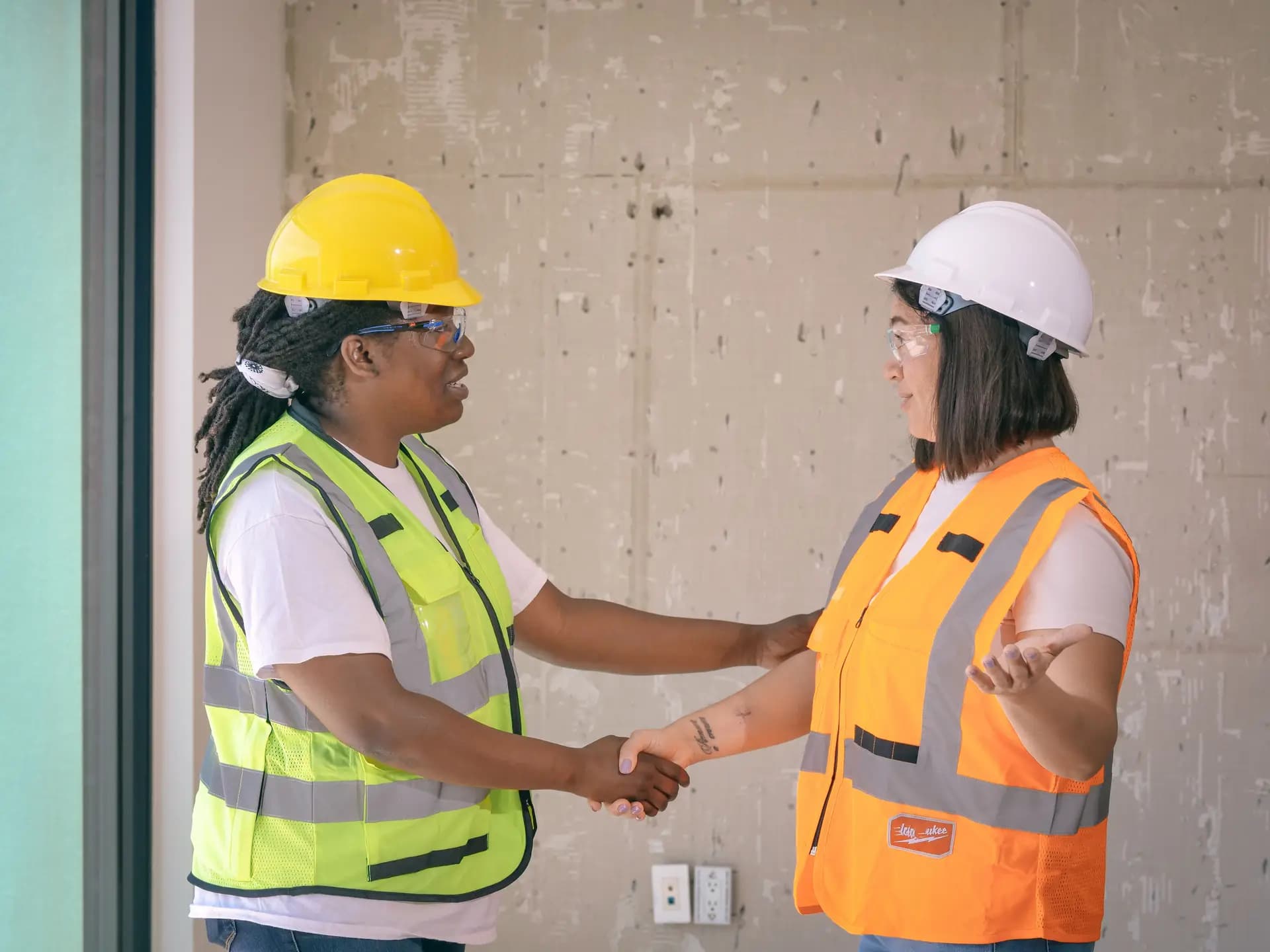 Two women in hard hats and hi-vis vests shaking hands at work
