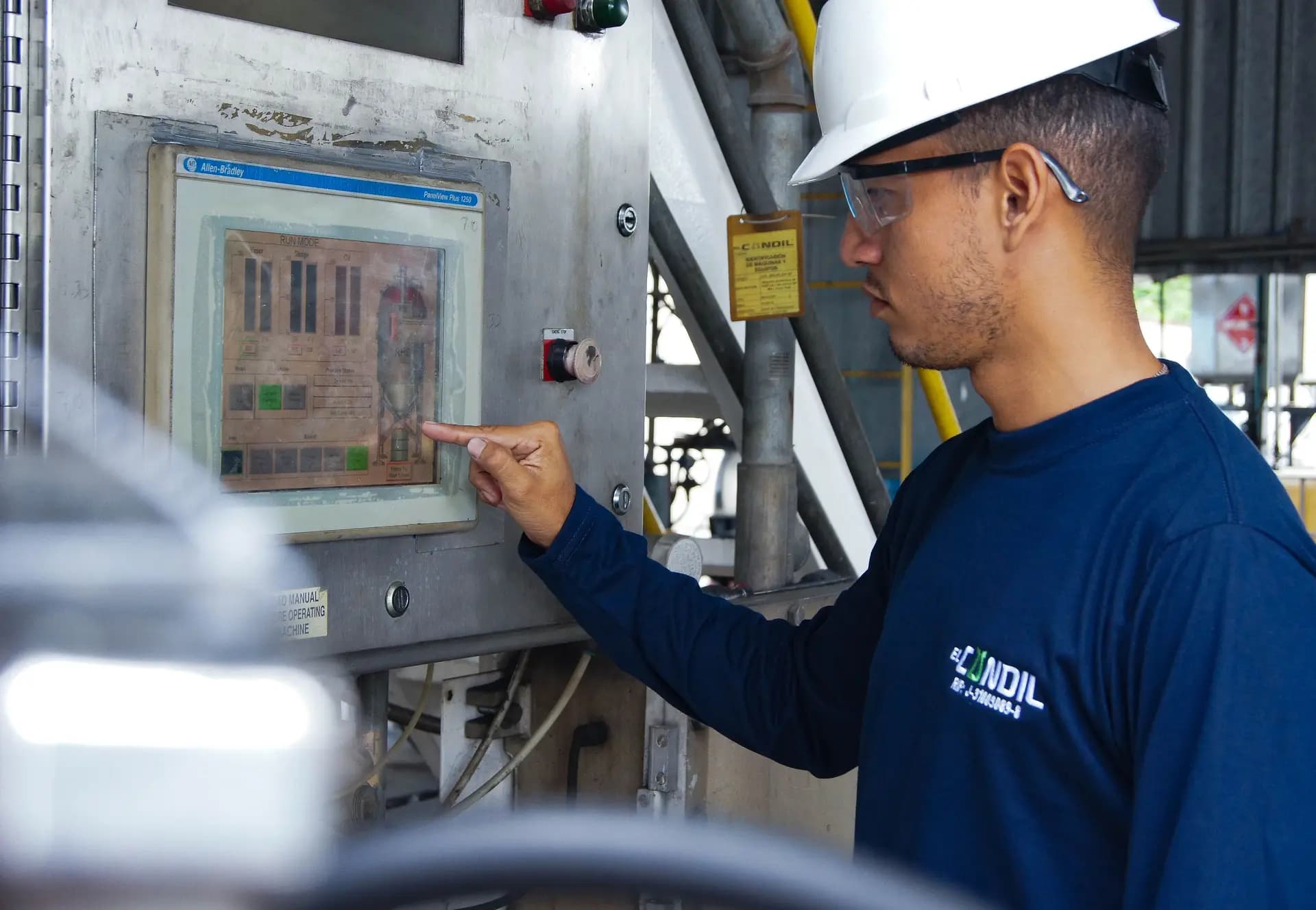 Engineer in a hard hat pointing at a touchscreen on a machine control panel