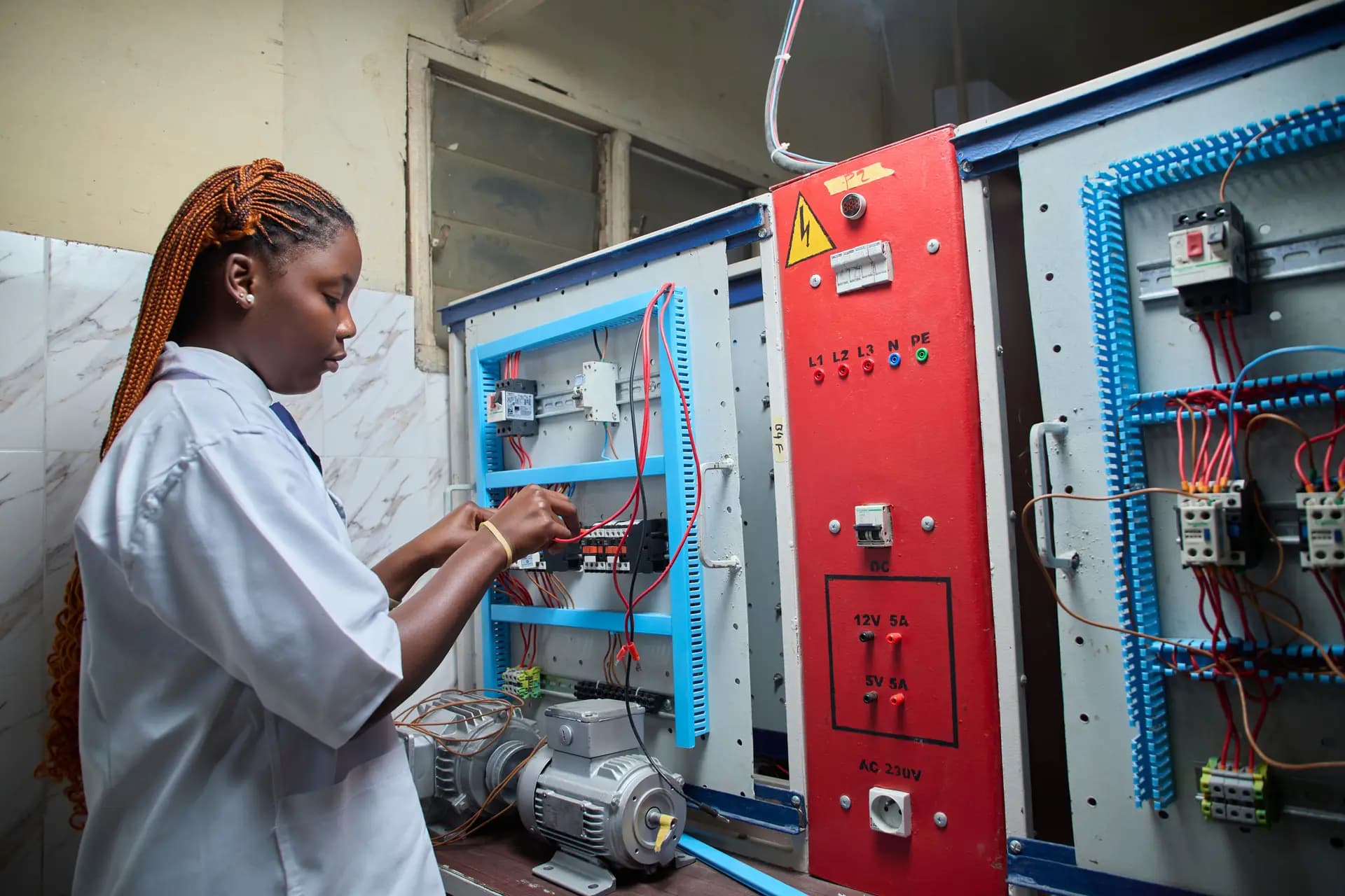 Woman technician in a lab coat working on a machine's electrical control cabinet