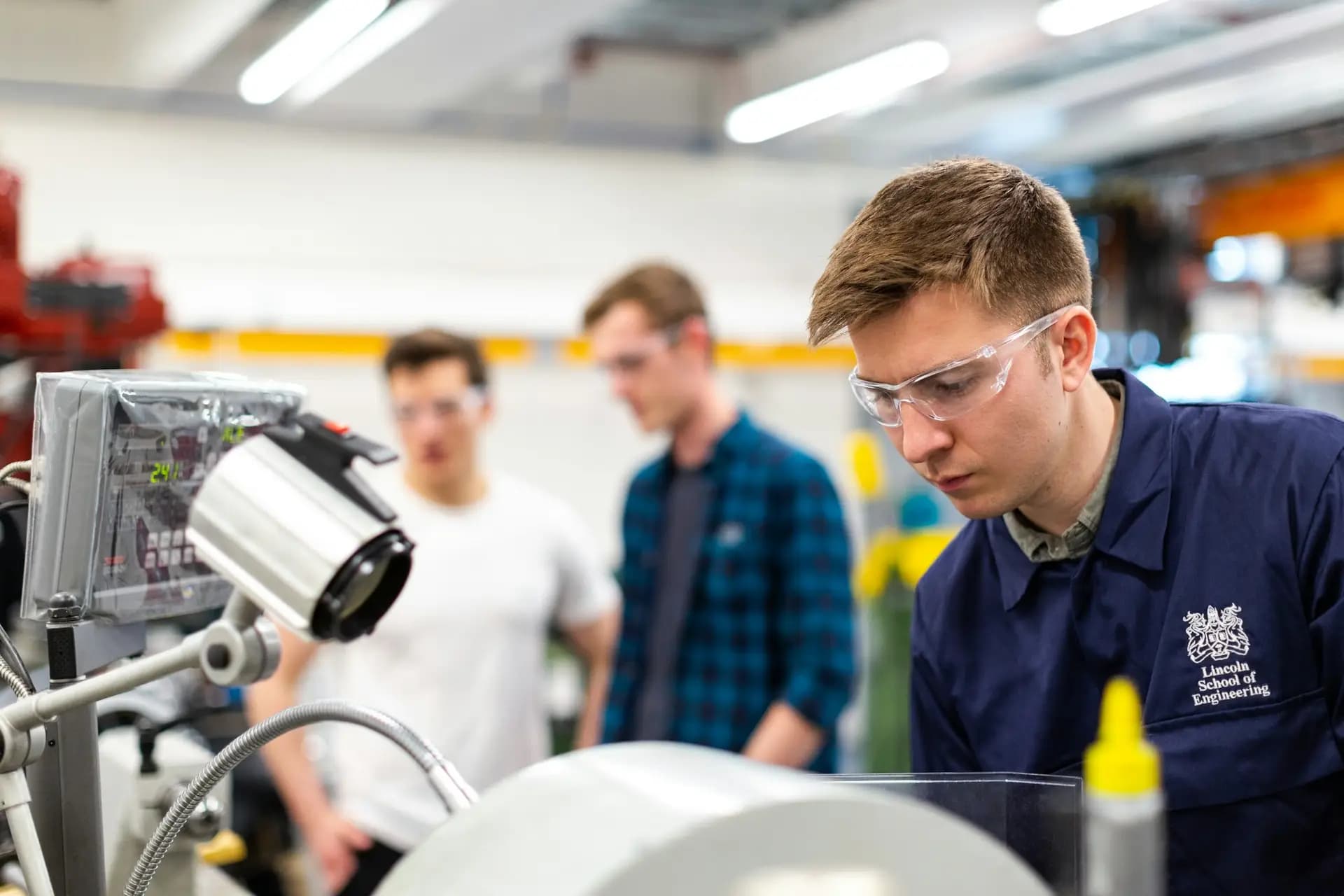 Trainee engineers in safety glasses working on equipment in a workshop