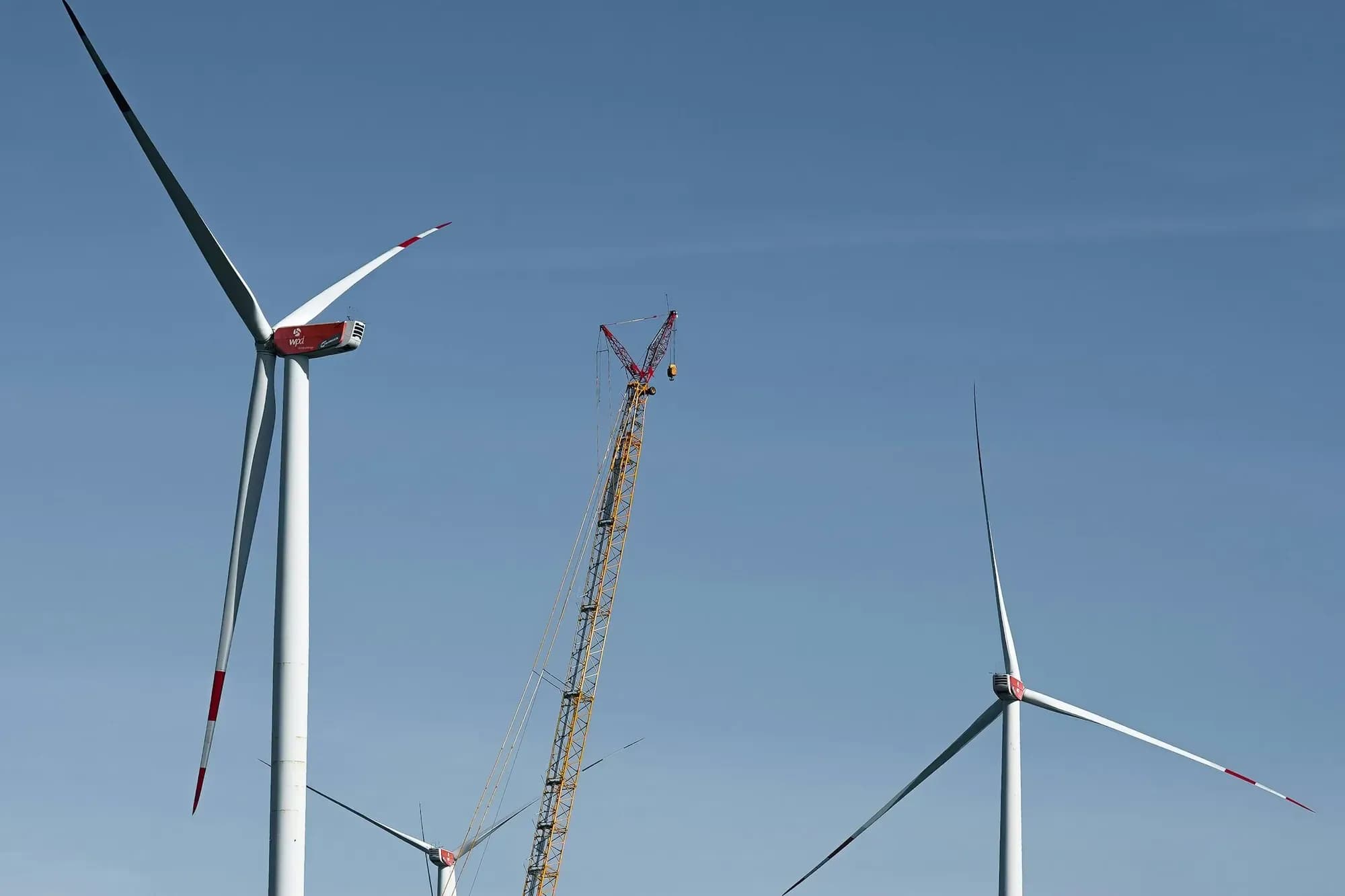 Crane assembling a wind turbine in a green field beside two finished turbines