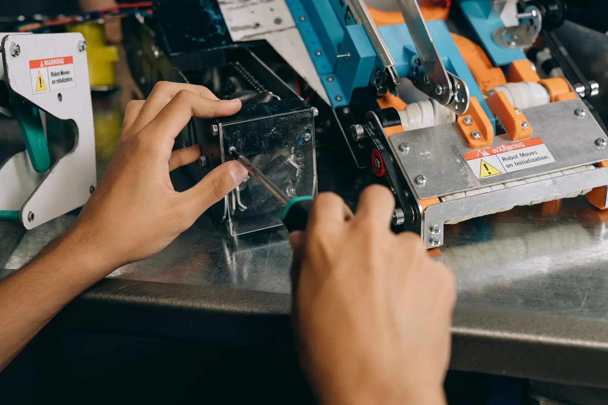 Hands using a screwdriver on the mechanism of a machine beside a robot warning label