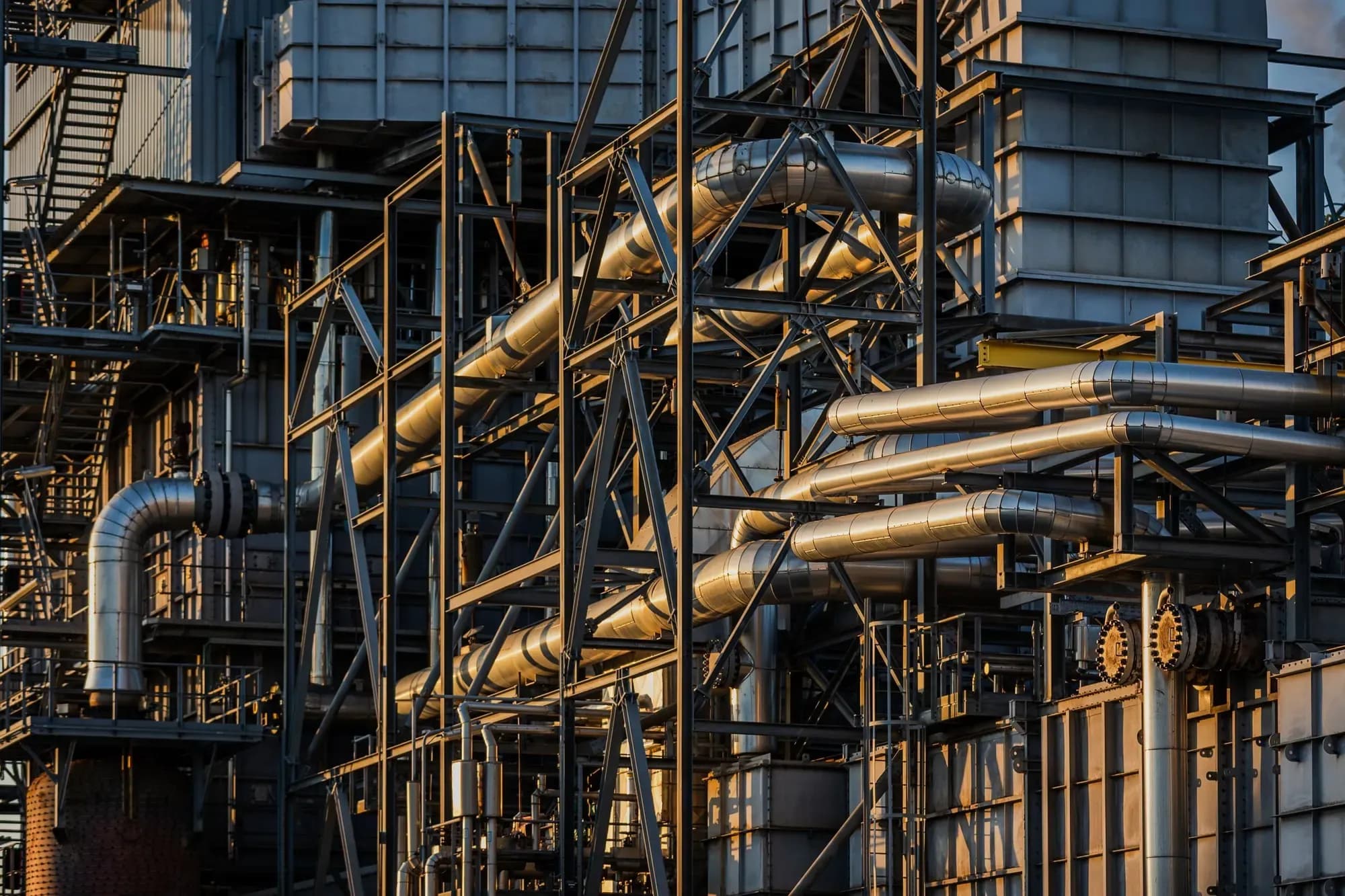 Gold-lit pipework and steel gantries of a process plant at Botlek, Rotterdam