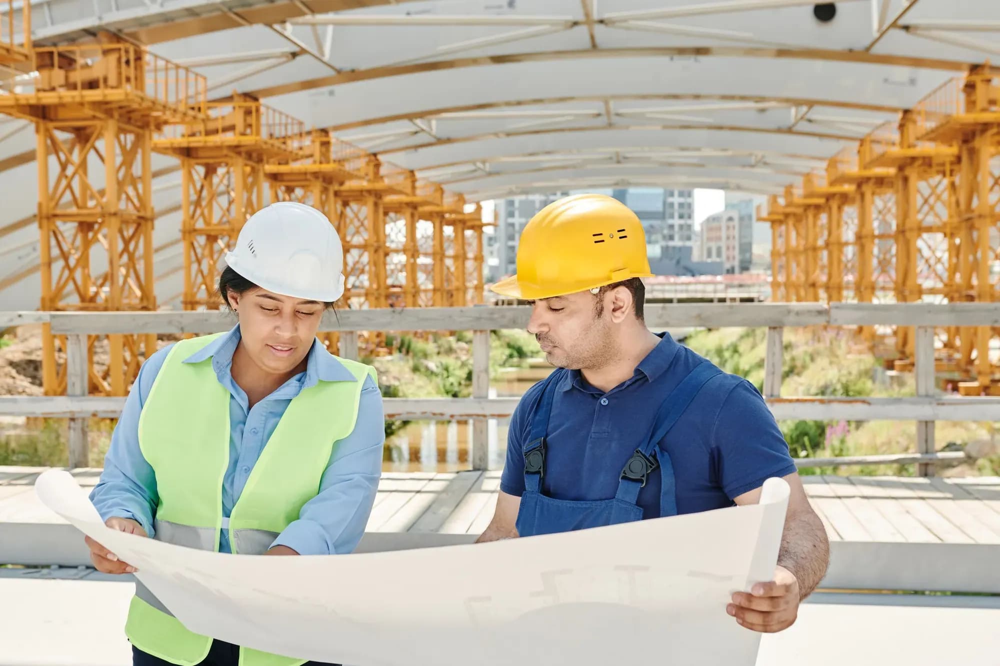 Two engineers in hi-vis and hard hats studying a large drawing on site