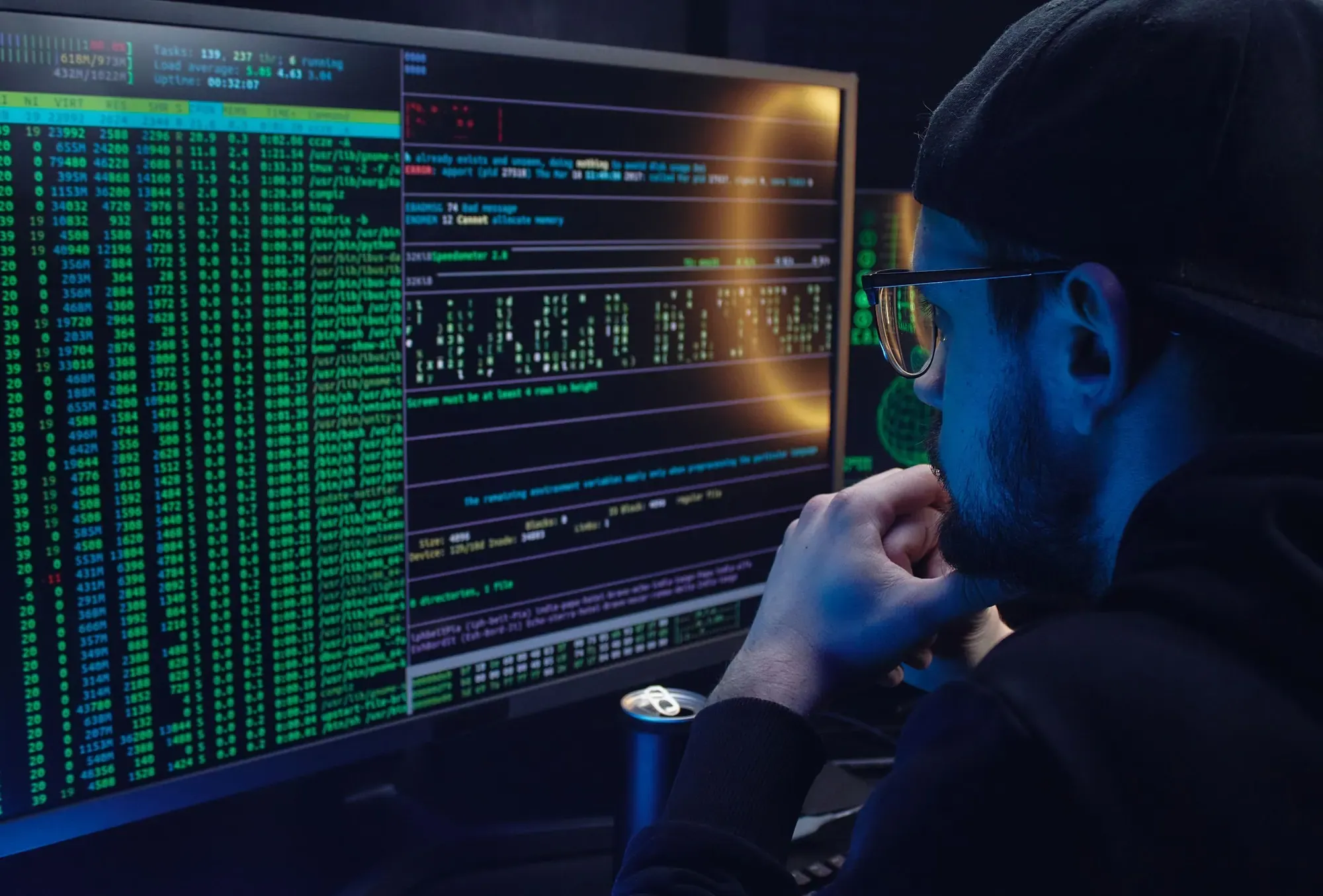 An engineer studying data and terminal output on a large monitor in a dim room