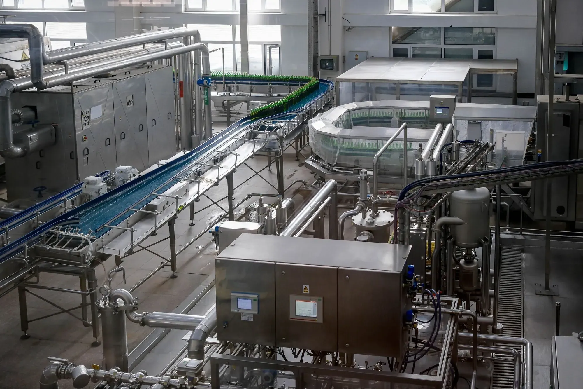 Bottling line with conveyors, tanks and control cabinets inside a beverage factory, a typical plant where PPM and breakdown cover are asked about