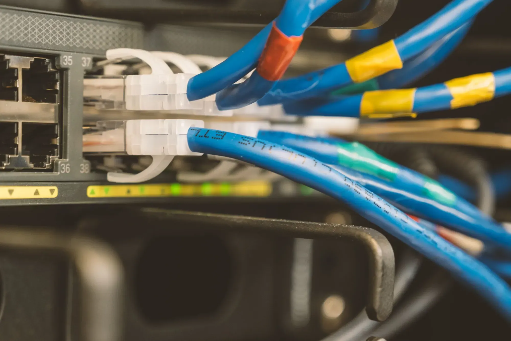 Close-up of blue Ethernet patch cables with coloured tape tags plugged into numbered switch ports