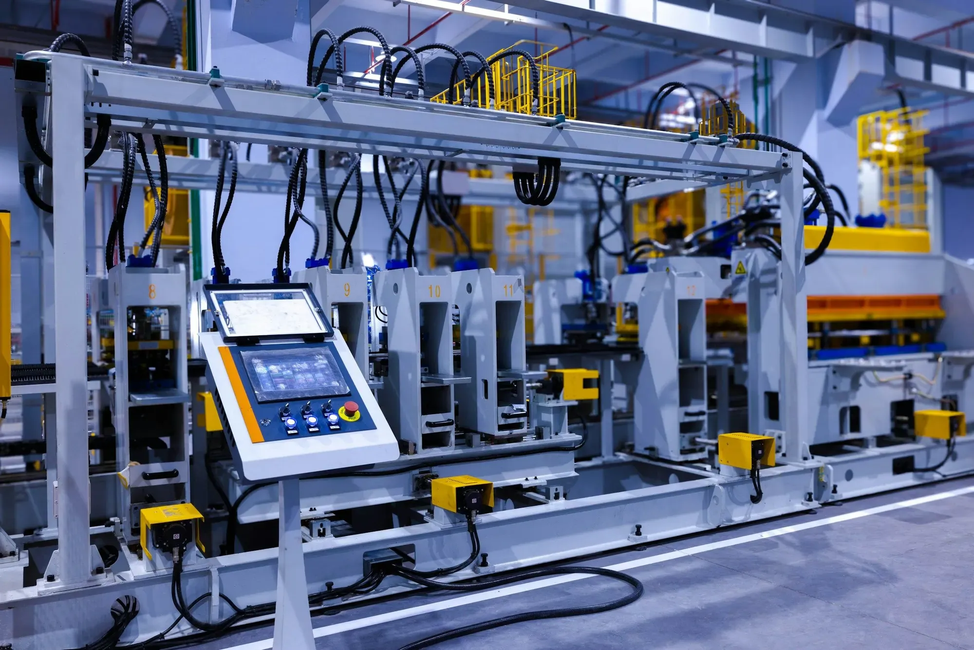 A factory machine line with a touchscreen control panel, a red emergency stop button and yellow safety sensor boxes along the frame