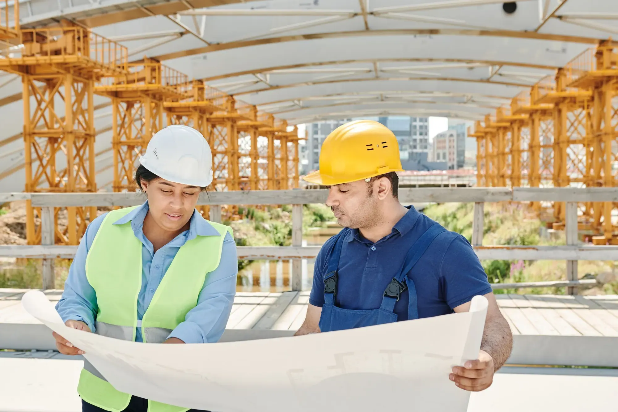 Two engineers in hi-vis and hard hats studying a large drawing on site